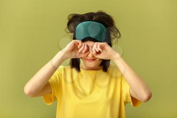 Sleepy young woman with mask on color background�