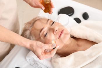 Mature woman undergoing treatment with face serum in beauty salon�