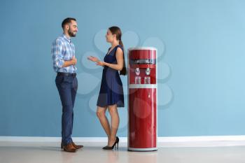 Man and woman near water cooler against color wall�