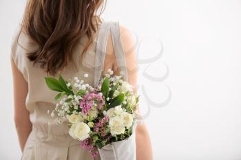 Young woman with bouquet of flowers in eco bag on light background�