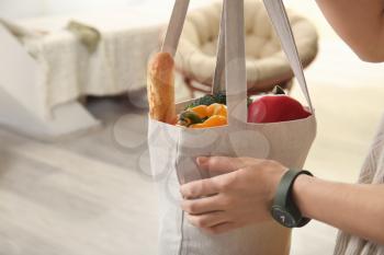 Young woman with fresh products in eco bag indoors�