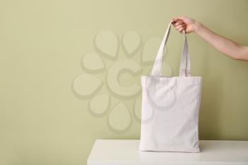 Female hand with eco bag on table against color background�