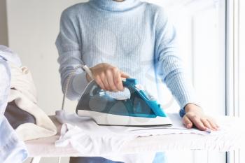 Young woman ironing clothes at home�
