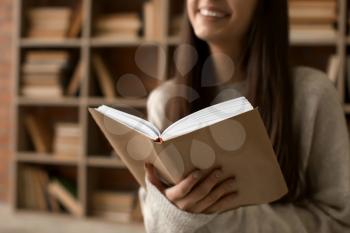 Beautiful young woman reading book in library, closeup�