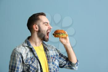 Man eating tasty burger on color background�