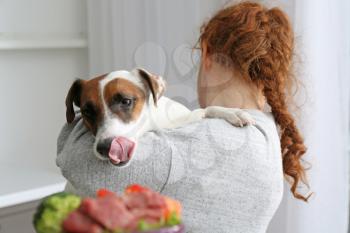 Woman holding cute funny dog looking at bowl with food�