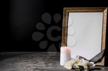 Blank funeral frame, candle and flowers on table against black background�