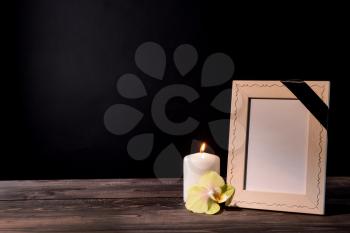 Blank funeral frame, candle and flower on table against black background�