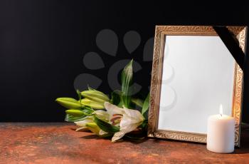 Blank funeral frame, candle and flowers on table against black background�