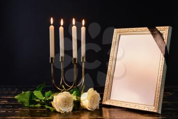 Blank funeral frame, candles and flowers on table against black background�