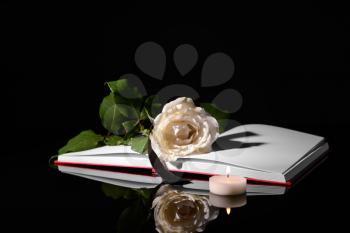 Open book, flower, black ribbon and burning candle on dark background�