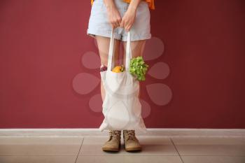 Young woman with vegetables in eco bag near color wall�