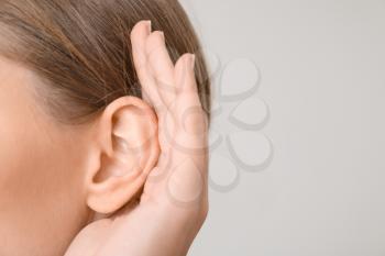 Young woman with hearing problem on light background, closeup�