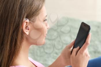 Young woman with hearing aid using mobile phone at home�