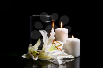 Mortuary urn, burning candles and lily flowers on dark background�