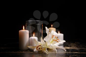Mortuary urn, burning candles and flowers on table against dark background�