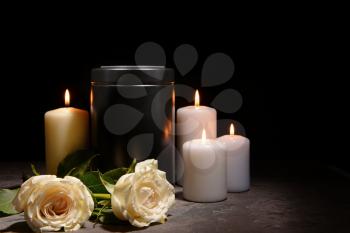 Mortuary urn, burning candles and flowers on table against dark background�