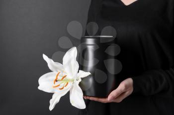 Woman with mortuary urn and lily flower on dark background, closeup�