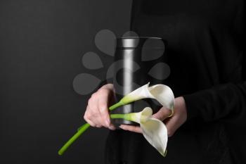 Woman with mortuary urn and flowers on dark background, closeup�