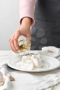 Woman pouring tasty olive oil onto feta cheese, closeup�