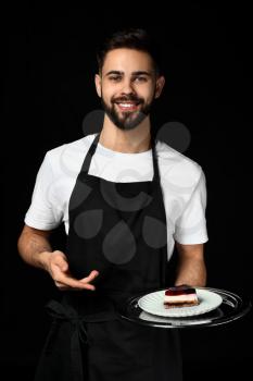 Handsome waiter with dessert on dark background�