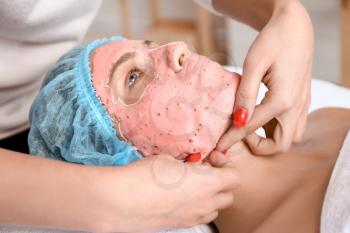 Cosmetologist removing alginate mask from young woman's face in beauty salon�