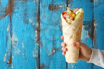 Female hand with tasty doner kebab on color wooden background�