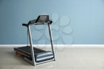 Modern treadmill near color wall in gym�