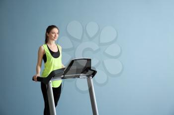 Sporty young woman training on treadmill against color background�