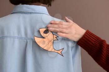 Woman sticking paper fish to her friend's back on color background. April Fool's Day prank�