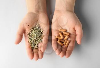 Female hands with plant based pills and dry herbs on white background�