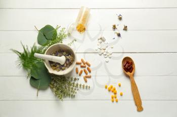Composition with mortar, herbs and plant based pills on white wooden background�