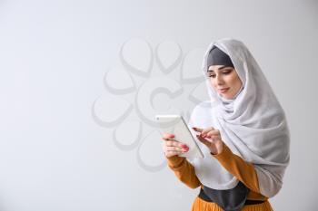 Young Muslim woman with tablet computer on light background�