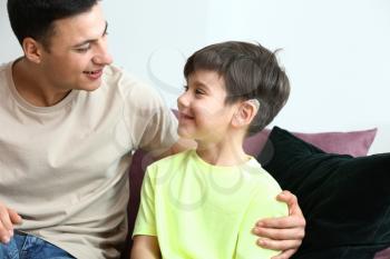 Young man and his son with hearing aid at home�