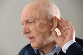 Senior man with hearing aid on light background�