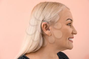Mature woman with hearing aid on color background�