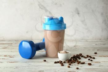 Bottle of protein shake with dumbbell on white wooden table�