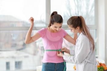 Nutritionist measuring waist of young woman in weight loss clinic�