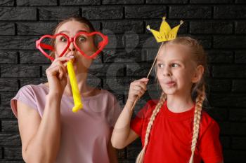 Woman and little girl in funny disguise on dark background. April fools' day celebration�
