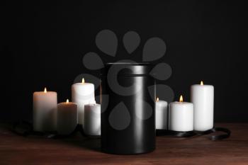 Mortuary urn with burning candles on table against dark background�