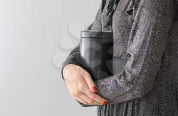 Woman with mortuary urn on light background�
