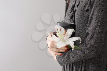 Woman with mortuary urn and lily flower on light background�