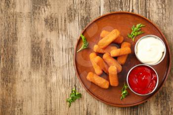 Plate with tasty mozzarella sticks and sauces on wooden table�