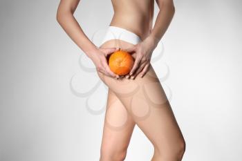 Beautiful young woman with orange on light background. Problem of cellulite�