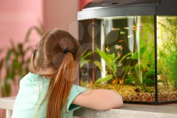 Cute little girl looking at fish in aquarium�