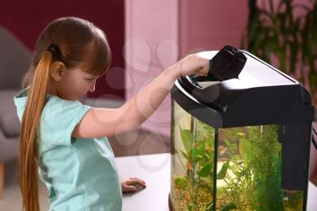 Cute little girl feeding fish in aquarium�