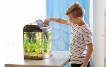 Cute little boy feeding fish in aquarium�