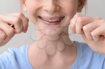 Smiling teenage girl with dental braces holding floss on grey background, closeup�