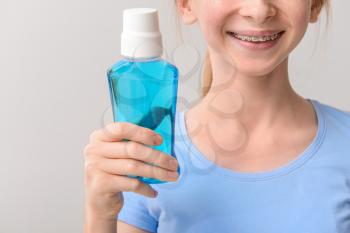 Smiling teenage girl with dental braces holding bottle of mouthwash on grey background�
