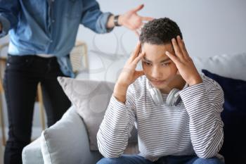 Sad African-American teenage boy having argument with his mother at home�